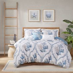 a bed with blue and white comforters in a room next to a plant on the floor