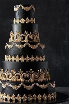 a black and gold wedding cake with intricate designs on it's tiered layers