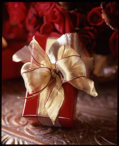 a red gift box with a gold bow on it sitting in front of some red roses