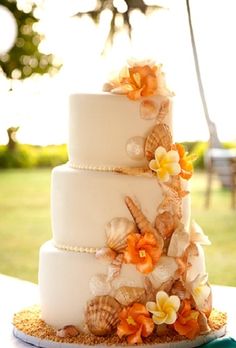 a white wedding cake with orange flowers and seashells