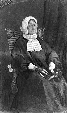 an old black and white photo of a woman sitting in a chair wearing a bonnet