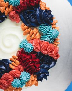 a cake decorated with colorful icing and flowers on top of a blue tablecloth