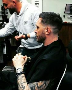 a man getting his hair cut at a barber shop with another man in the background