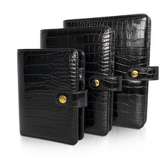 three black alligator skin leather cases with gold buttons on the front and back, all lined up against each other