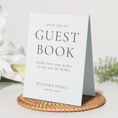 a white guest book sitting on top of a wicker basket next to some flowers