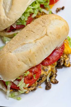 two sub sandwiches with lettuce, tomato and other toppings on a white plate