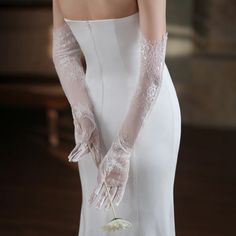 a woman in a white wedding dress with gloves on her arm and holding a flower