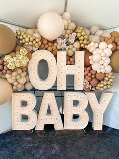 the letters oh baby are surrounded by balloons and streamers in gold, white, and beige colors