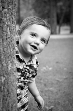 a black and white photo of a young boy leaning against a tree in the park