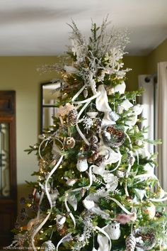 a decorated christmas tree with white ribbons and ornaments on it in a living room area