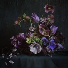 an arrangement of purple and green flowers on a black tablecloth with dark wall in the background