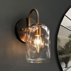 a light that is on the side of a wall next to a mirror with a tree in it