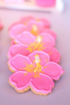 pink and yellow decorated cookies sitting on top of a purple tablecloth with flowers in the middle