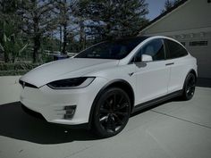 a white tesla model x parked in front of a garage with black wheels and rims