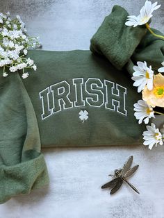 a green towel with the word irish on it next to flowers and a dragonfly