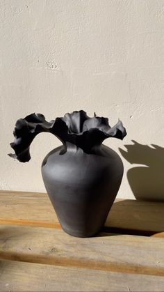 a black vase sitting on top of a wooden table next to a shadow of a plant