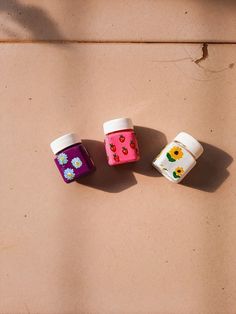 three small jars sitting on top of a brown floor next to each other with flowers painted on them