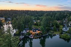 an aerial view of a lake surrounded by trees and houses at dusk with the sun setting in the distance