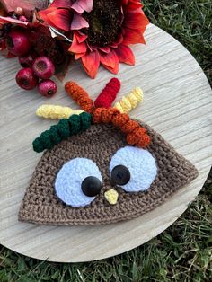 a crocheted turkey hat on top of a wooden board with flowers in the background