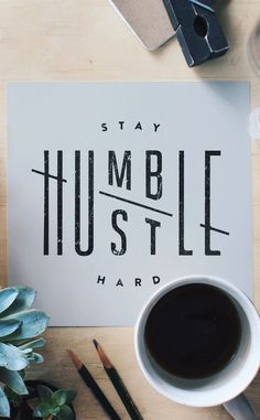 a cup of coffee sitting on top of a table next to a sign that says, stay humble hustle hard