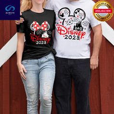 a man and woman standing next to each other in front of a wooden fence wearing mickey mouse shirts