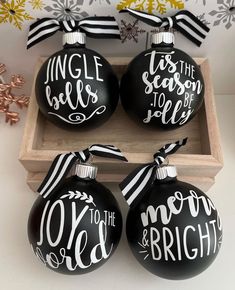 three black ornaments with white lettering are sitting in a wooden box next to snowflakes