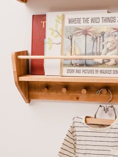 there is a wooden shelf with books on it and a t - shirt hanging from the wall