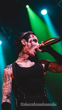 a man with tattoos and piercings on his face holding a microphone in front of green lights