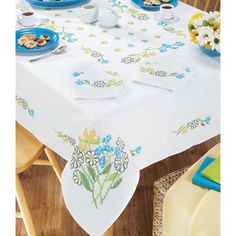 a white table with blue and yellow flowers on it is surrounded by plates of food