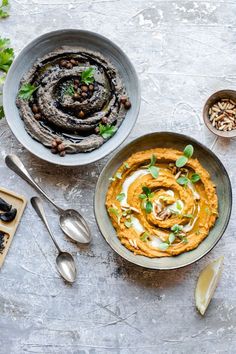 two bowls filled with hummus and other food items on top of a gray table