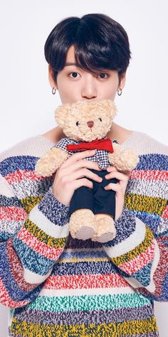 a woman holding a teddy bear in her hands and wearing a sweater over her shoulders