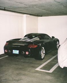 two black sports cars parked in a parking space with white walls and concrete flooring