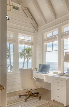 a white desk and chair in a room with large windows looking out to the ocean