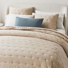 a bed with white and blue pillows on top of it next to a night stand