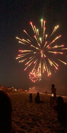 fireworks are lit up in the night sky above people sitting and standing on the beach