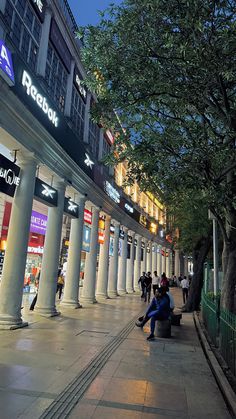 people are sitting on benches in the middle of an empty city street at night time