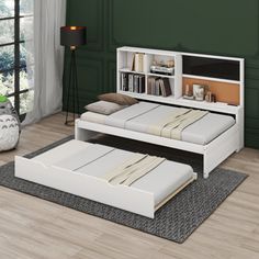 a white bed sitting on top of a wooden floor next to a book shelf filled with books