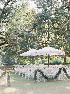 an outdoor ceremony setup with white chairs and umbrellas