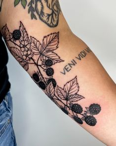 a person with a tattoo on their arm that has berries and leaves all over it