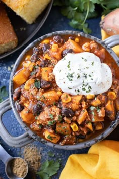 a bowl filled with chili and beans next to bread, cilantro and sour cream