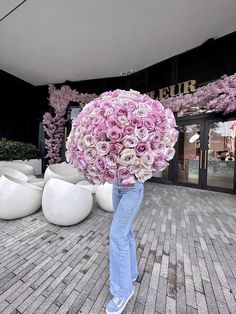 a person holding a large bouquet of flowers in front of a storefront with pink flowers on it