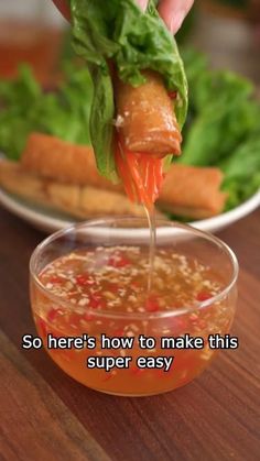 someone is dipping some food into a small glass bowl on a table with lettuce and carrots