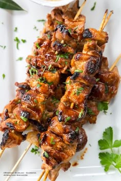 chicken skewers with sauce and parsley on a white plate