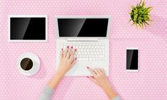 a woman using a laptop computer on top of a pink table next to two coffee mugs