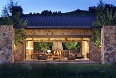 an outdoor living area with stone walls and patio furniture at night, surrounded by greenery