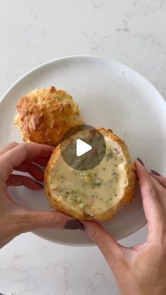 a person holding a piece of food in their hand on a white plate with a biscuit