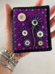 a woman's hand holding a small purple case with buttons and beads on it