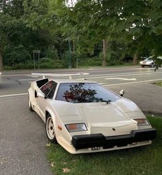 a white sports car parked on the side of the road in front of a tree