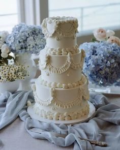 a white wedding cake sitting on top of a table next to blue and white flowers