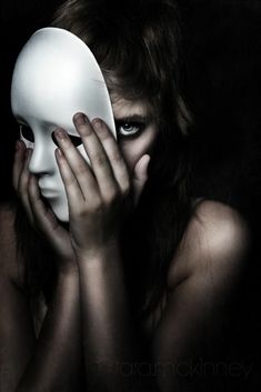 a woman holding a white mask over her face with both hands and covering it's face